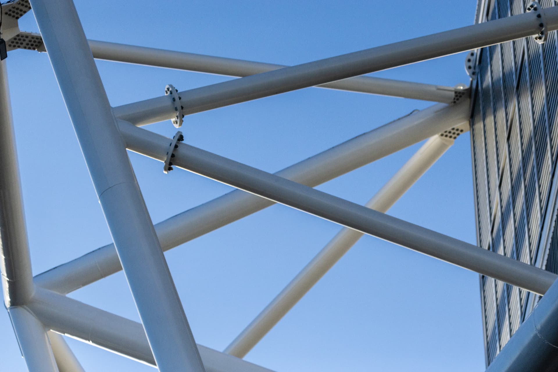 The steel beams of a stadium criss-crossing against a blue sky.