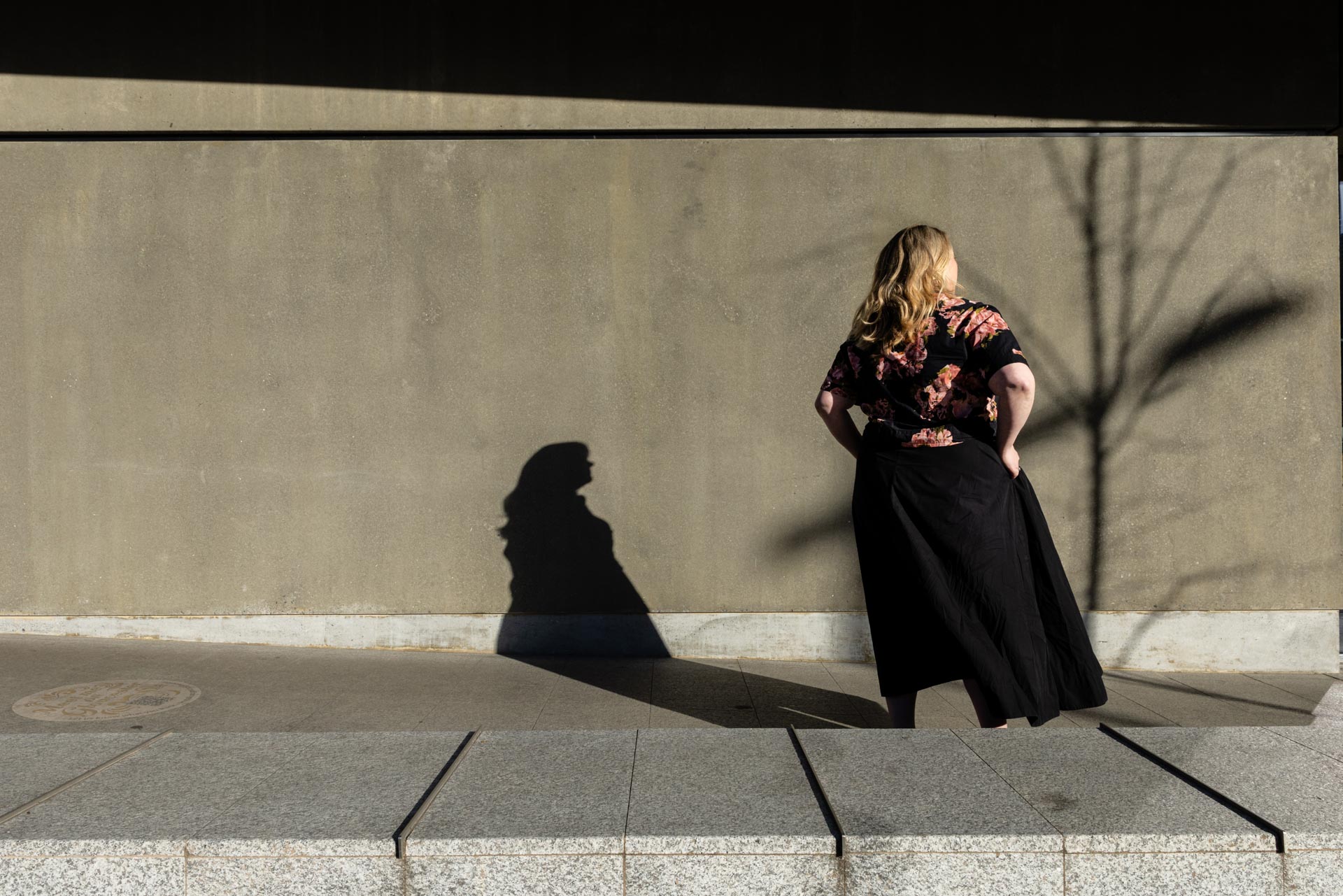 Camille standing against a concrete wall, her shadow cast beside her