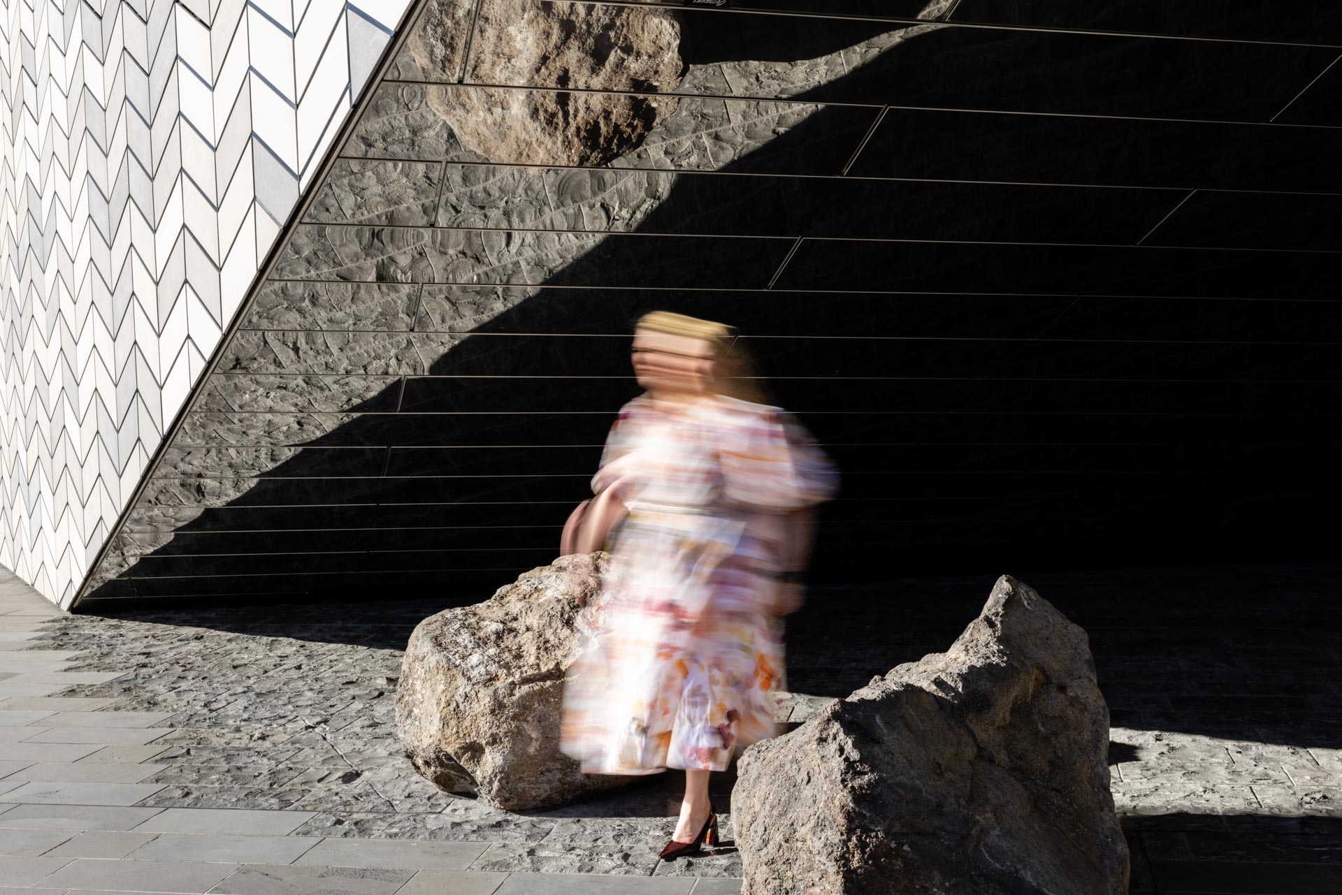 Camille Hughes stepping between large rocks on a city street, her patterned dress blurred with movement