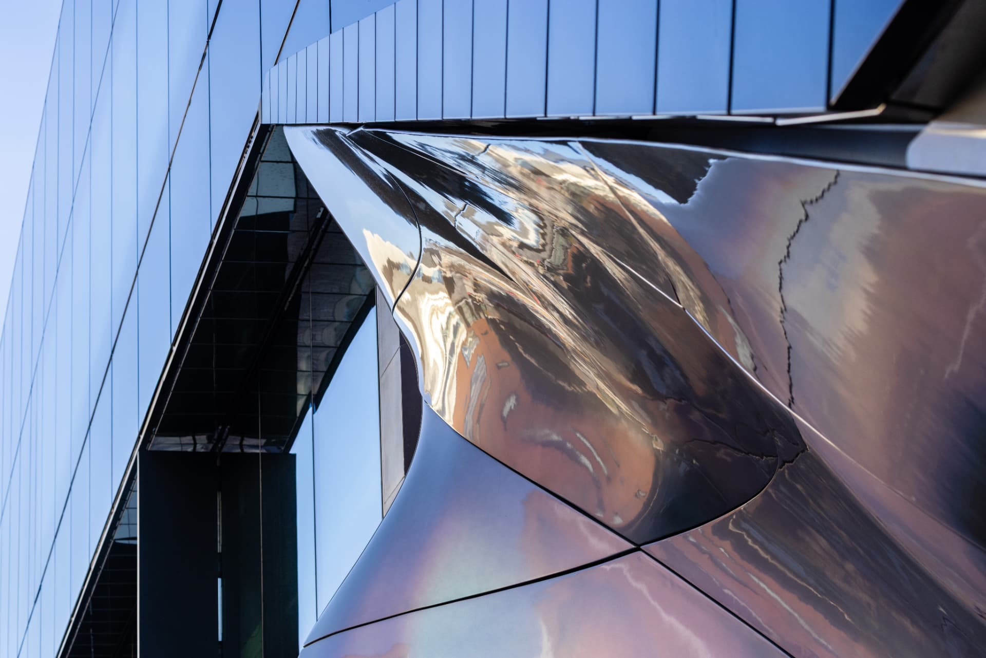 Curved mirror-polished metal facade against a blue sky