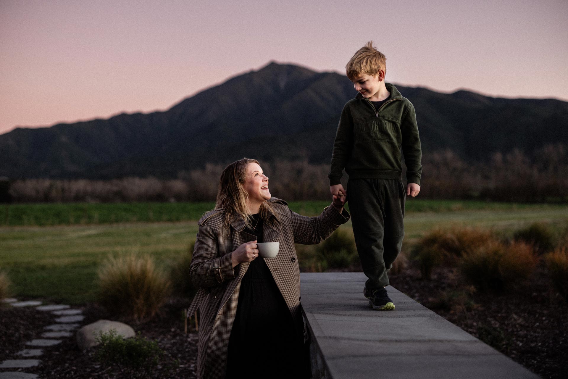 Camille walking hand in hand with her son at dusk, mountains behind them